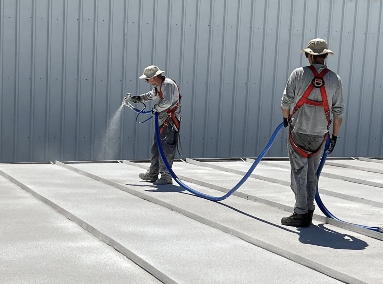 Crew spraying cork coating across a metal roof
