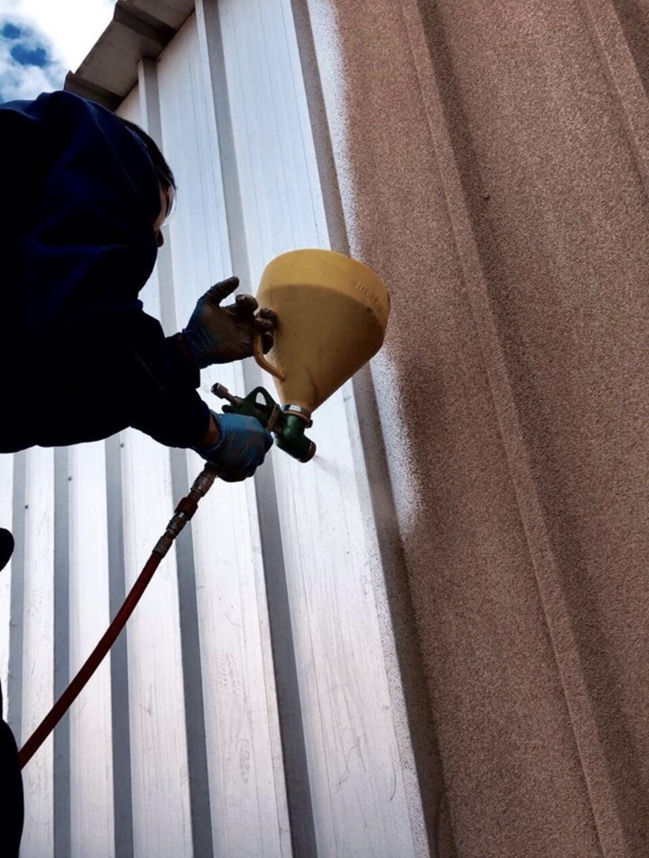 Applicator spraying cork coating onto profiled metal cladding